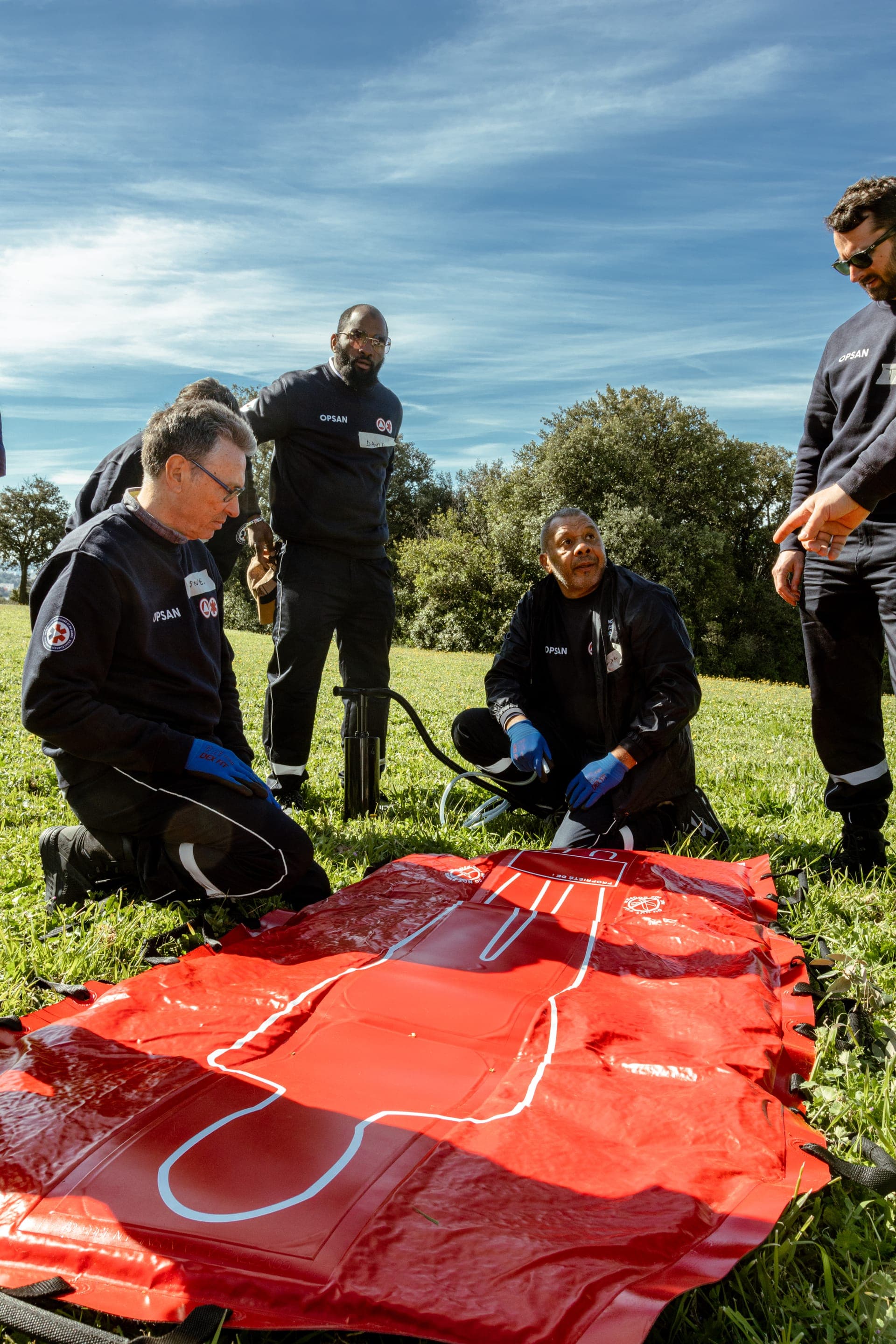 Cinq bénévoles OPSAN autour d'un matelas immobilisateur rouge en extérieur