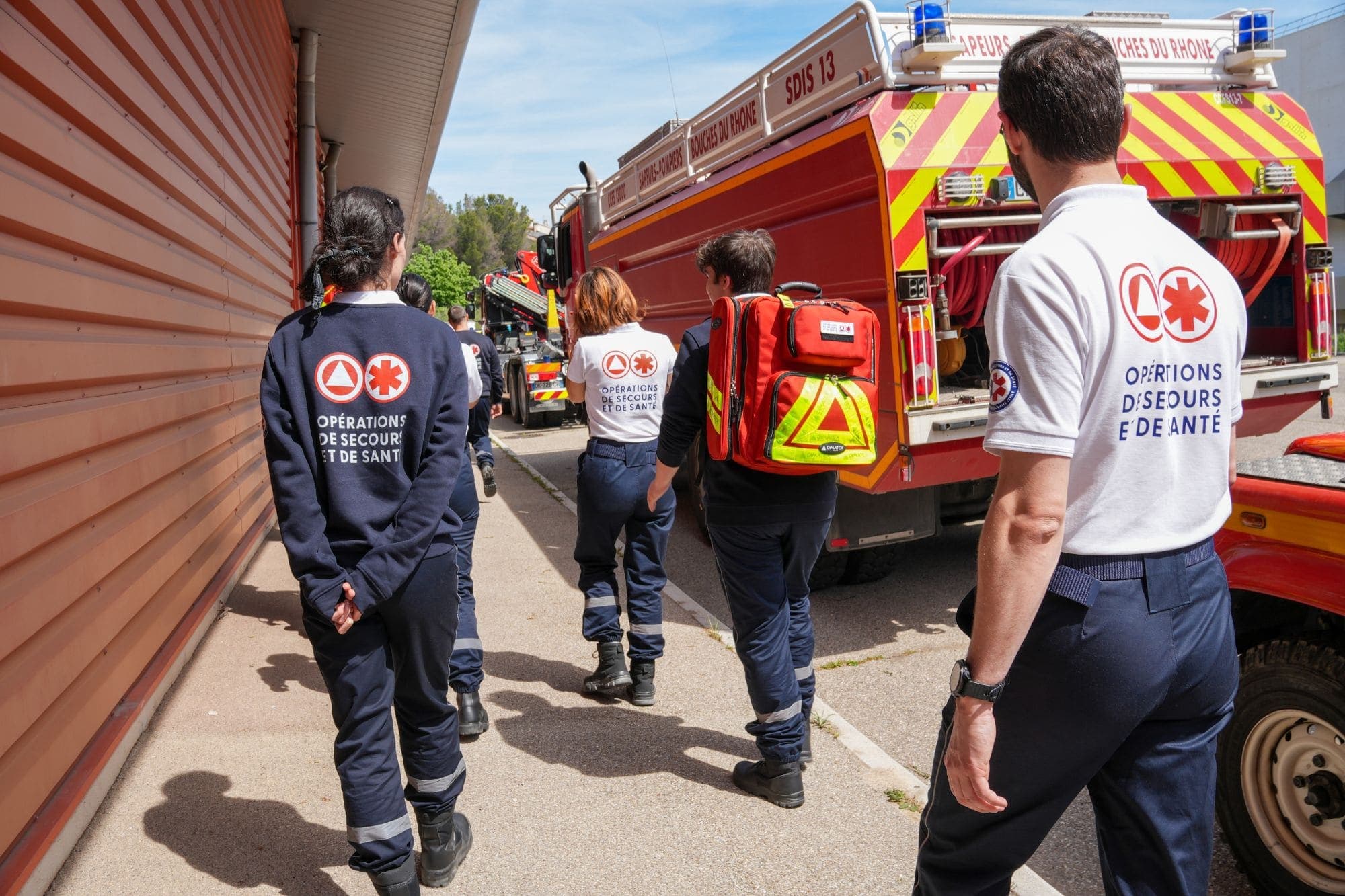 Équipiers OPSAN longeant un camion des Sapeurs-Pompiers des Bouches-du-Rhône, sac d'intervention sur le dos