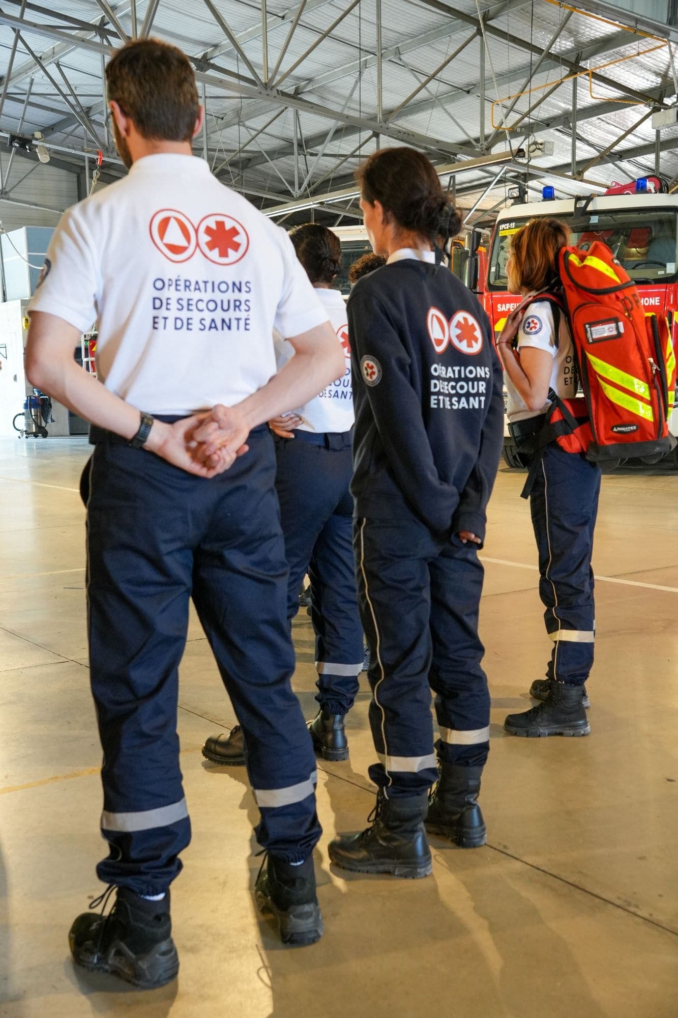 Secouristes OPSAN rassemblés dans la remise d'une caserne devant les engins des Sapeurs-Pompiers